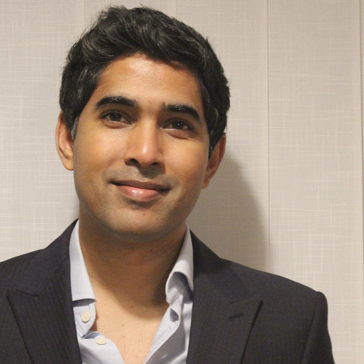 Humayon Pramanik, an Asian man, with short dark hair, smiles at the camera. He wears an open necked grey shirt and dark blazer